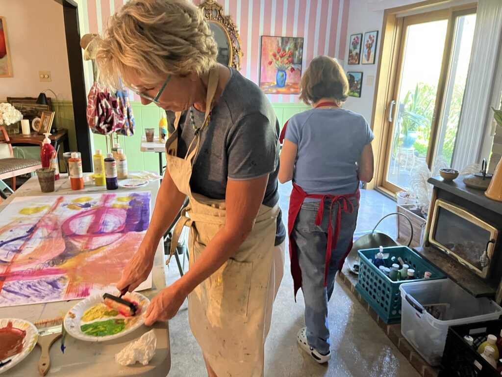 An adult artist painting a colorful abstract acrylic piece on paper in a well-lit studio