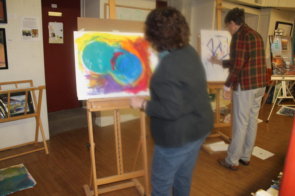 Woman with dark grey sweat shirt seen on the back painting on an easel an intuitive painting.