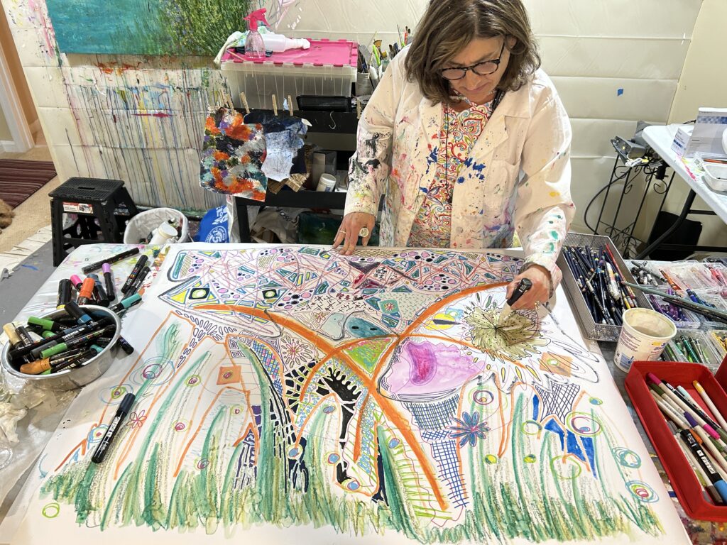 A student is standing bent over behind a table with a large piece of paper where she's painting on.