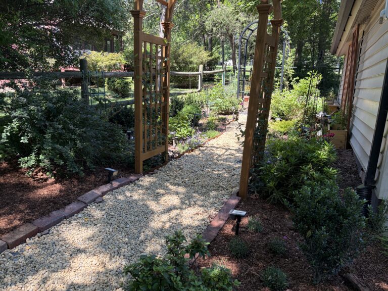 river rock garden path under an arbor with flower beds on the sides.