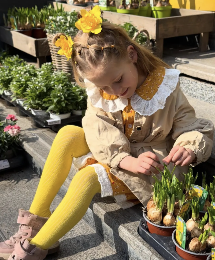 Girl with a yellow bow in her hair and yellow tights looking down on a basket with onions.