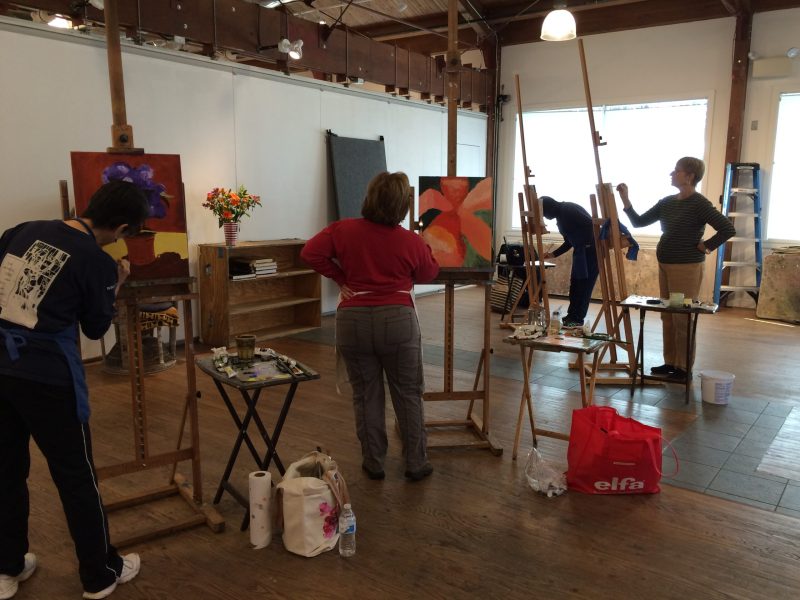 Adult art class in session with students focused on painting techniques in natural light studio